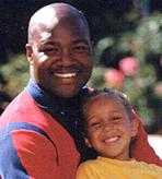 Picture of a father and his young daughter sitting outside, smiling.
